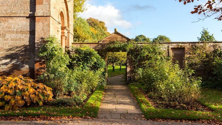 Stone pathway leading through a garden gate beside Acorn Bank's building, surrounded by autumn foliage